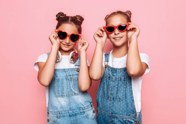 Two stylish teenage girls in sunglasses posing on a pink background