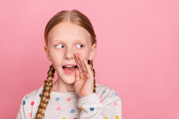 Photo of charming tricky school girl wear pullover arm mouth telling you secret looking empty space isolated pink color background.